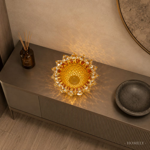 Decorative glass bowl on a wooden surface with a warm glow, surrounded by a bottle and a dark dish.