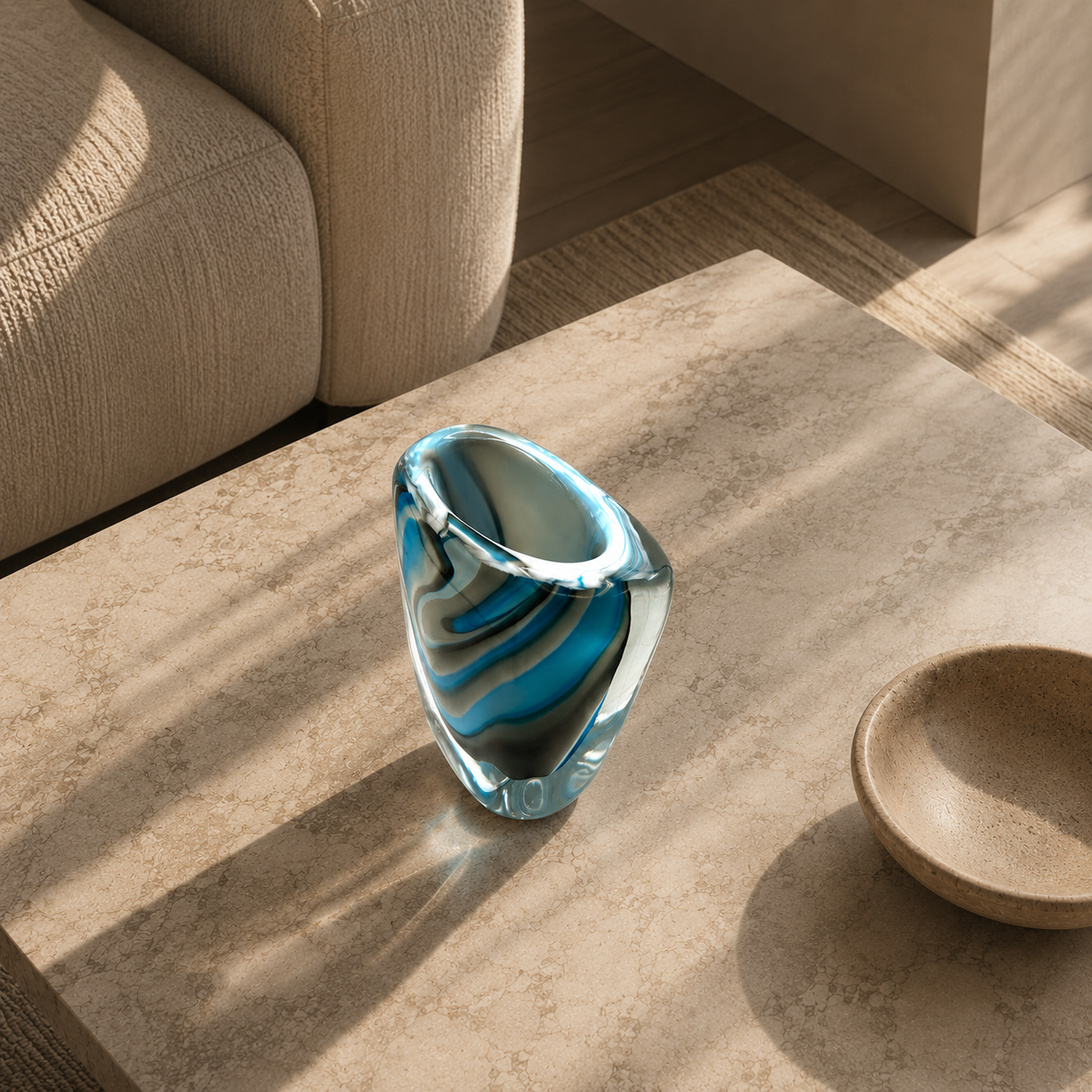 Blue glass vase on a stone surface with a beige sofa in the background