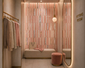 Fitting room with pink and gold decor, including a mirror, bench, and clothes rack.