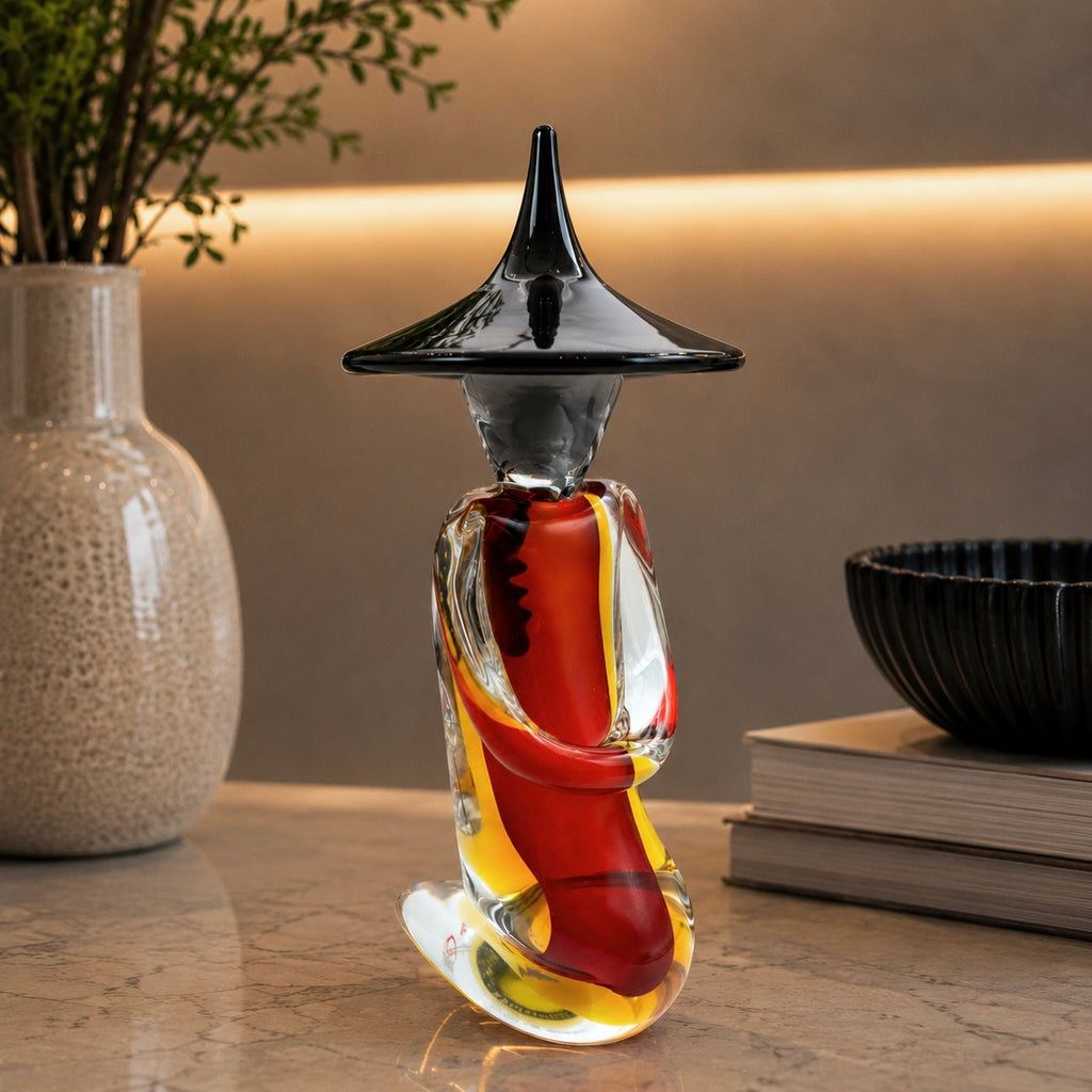 Decorative glass sculpture of a boot with a black hat on a wooden surface.