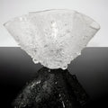 Glass sculpture on a reflective black surface with a gray background