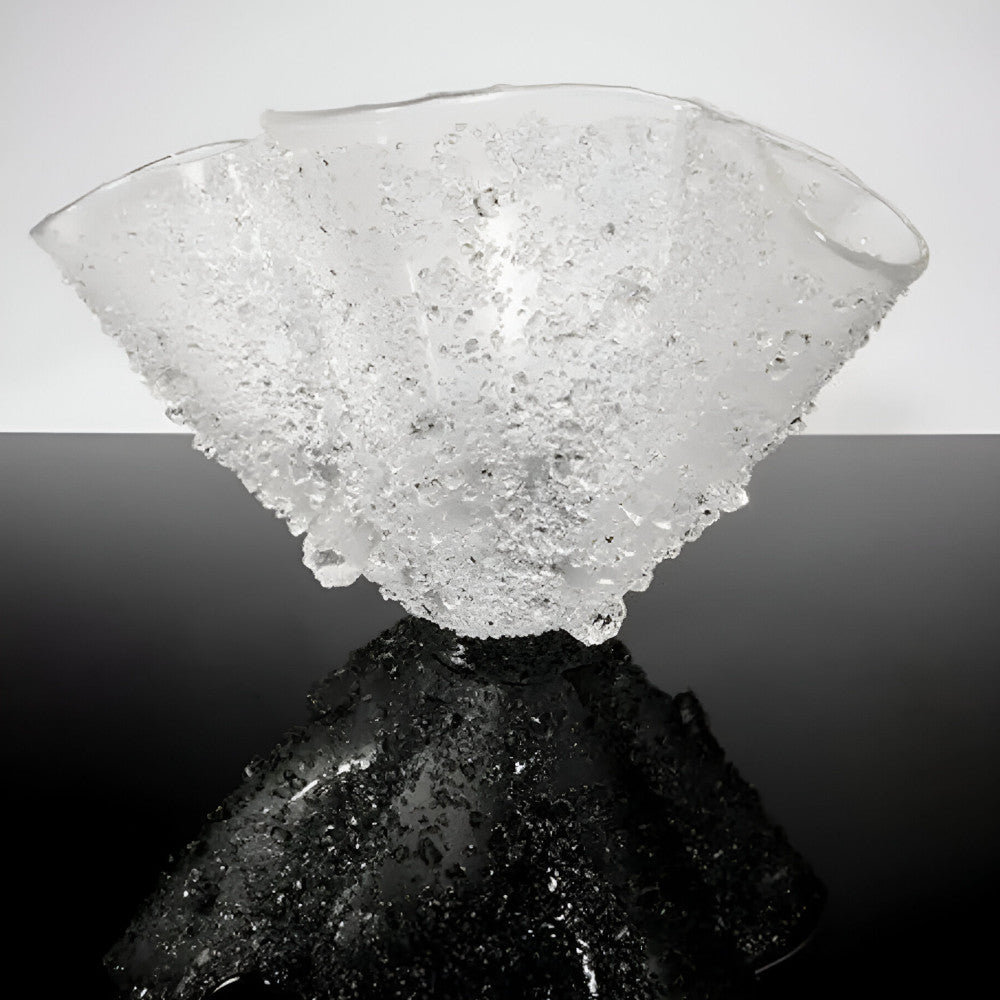 Glass sculpture on a reflective black surface with a gray background