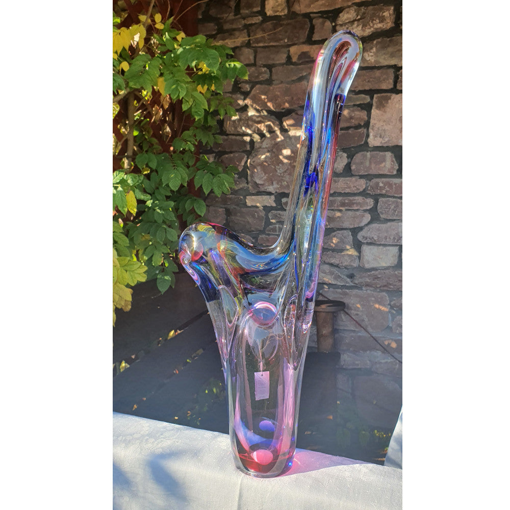 Colorful glass sculpture on a stone surface with plants in the background