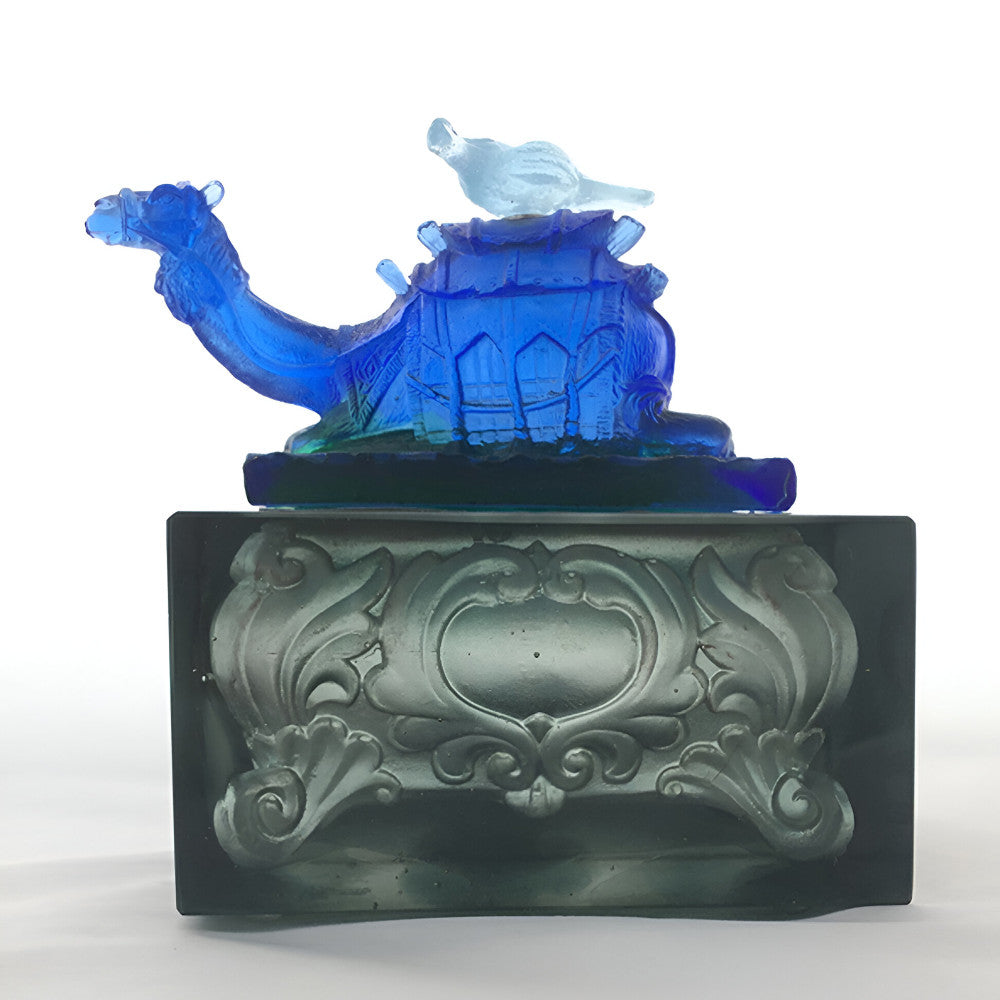Decorative glass sculpture of a ship with a bird on top, placed on an ornate base.