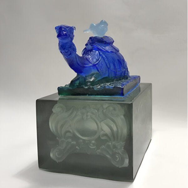 Blue glass sculpture on a gray pedestal with a white background