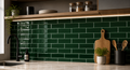 Kitchen with green tiled backsplash, wooden cutting board, and potted plants.