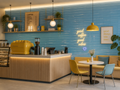 Modern coffee shop interior with blue tiled wall, yellow coffee machine, and seating area.
