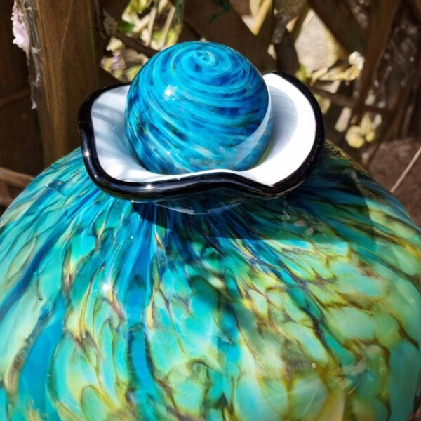 Decorative glass object with blue and green swirls on a white base
