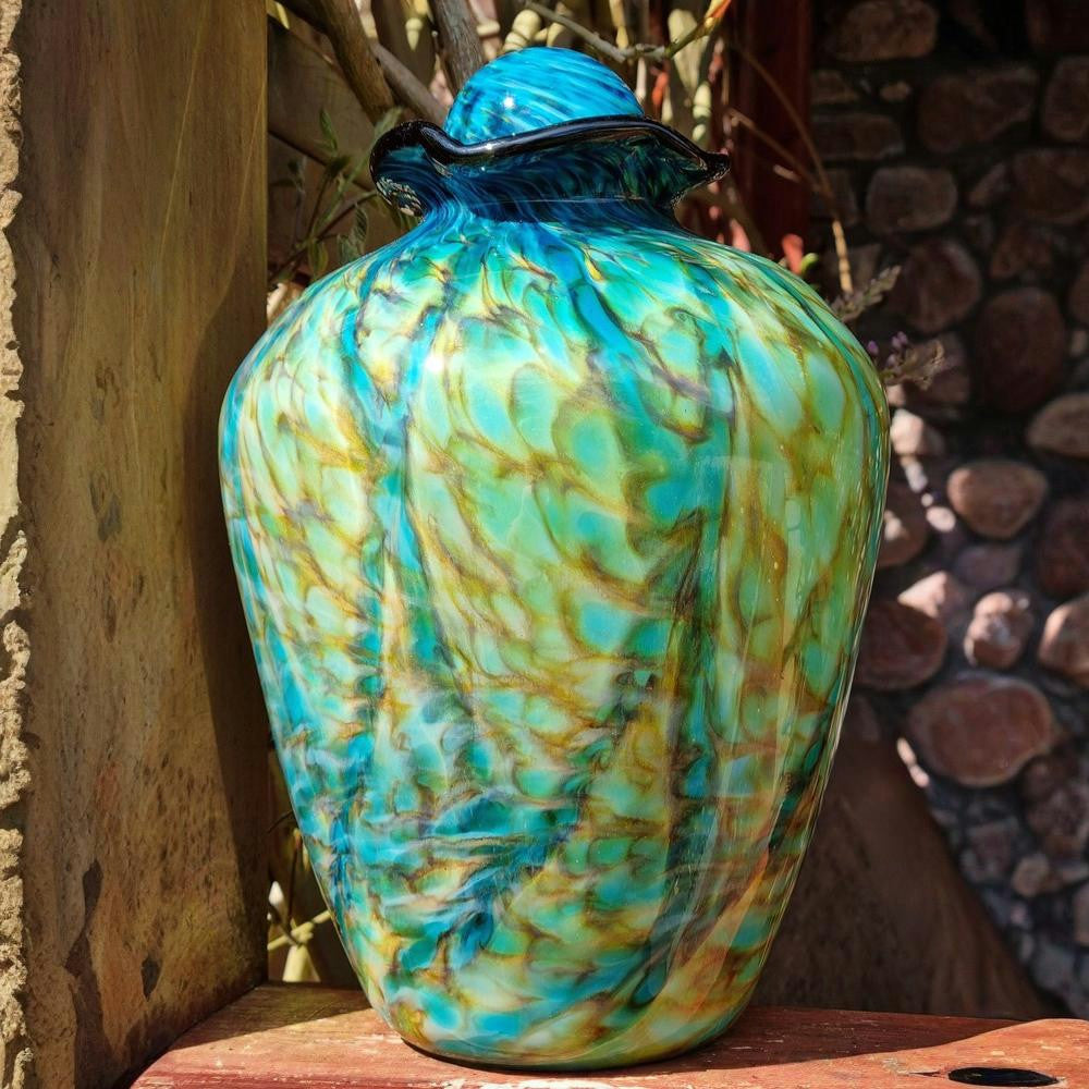 Decorative glass vase with blue and green patterns on a wooden surface.
