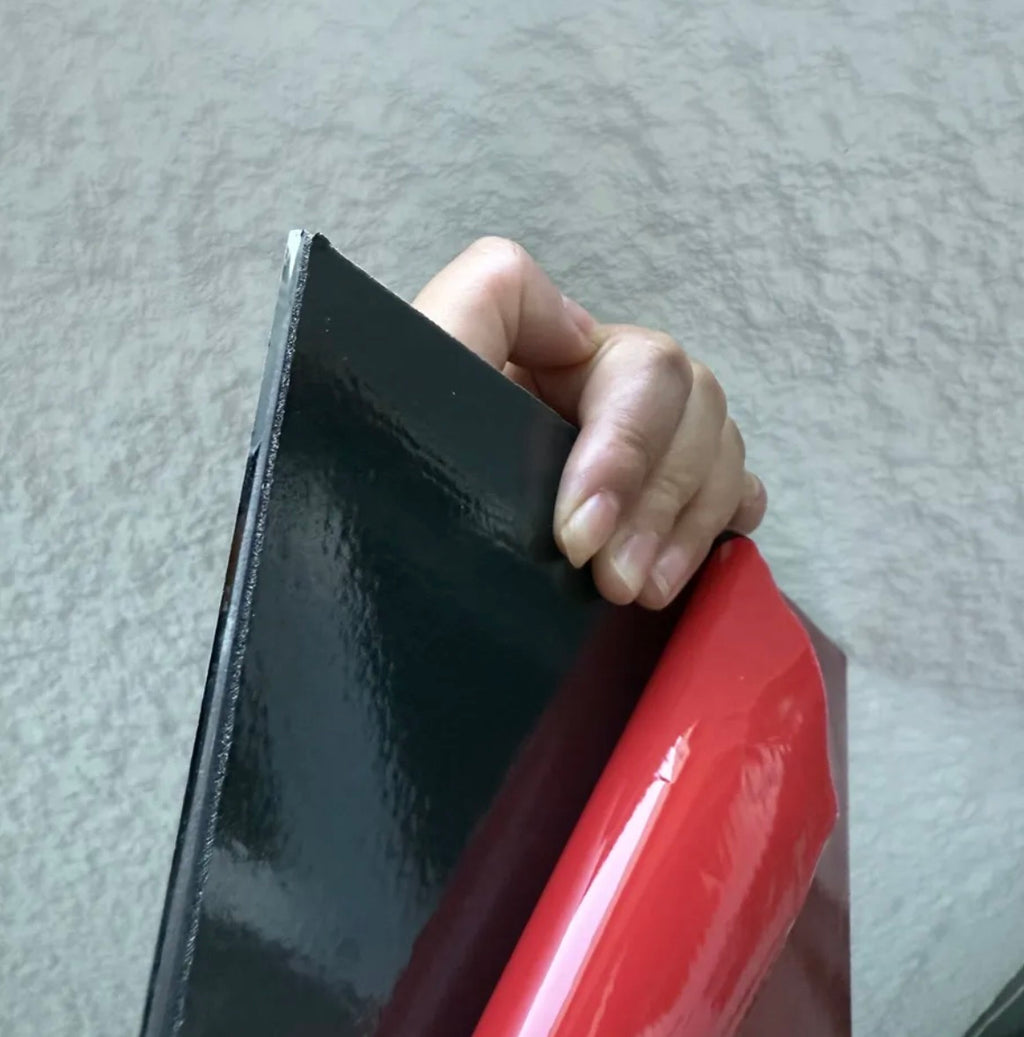 Hand holding a black object against a gray wall