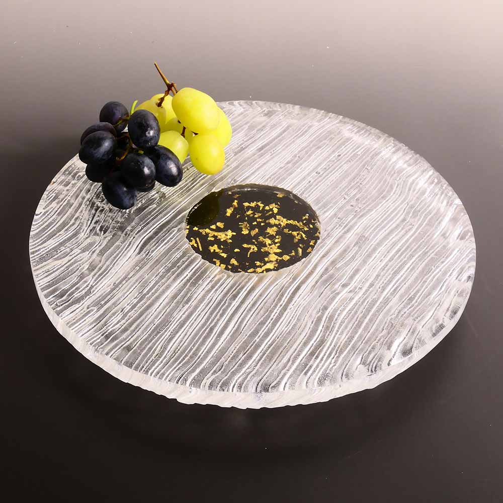 Round glass tray with decorative edge, black center, and fruit on a dark background