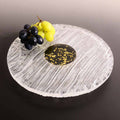 Round glass tray with decorative edge, black center, and fruit on a dark background