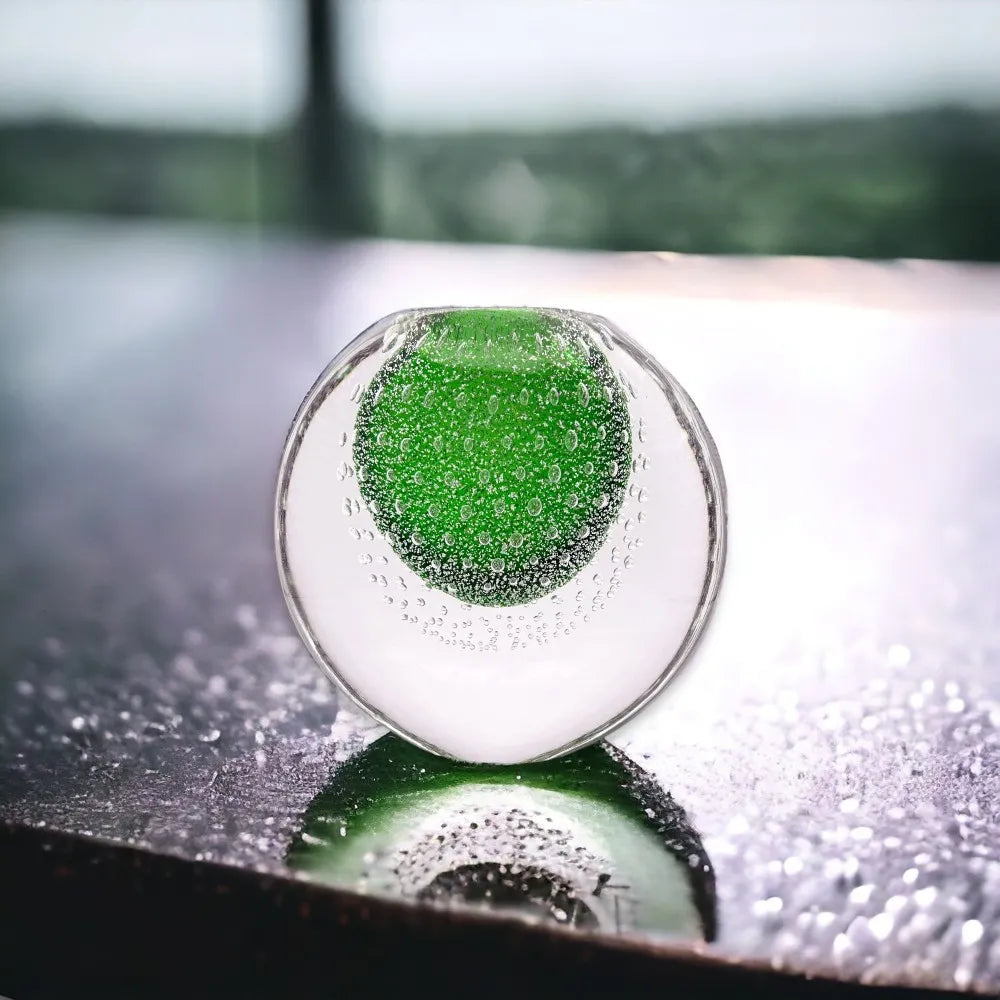 Green object inside a transparent sphere on a reflective surface